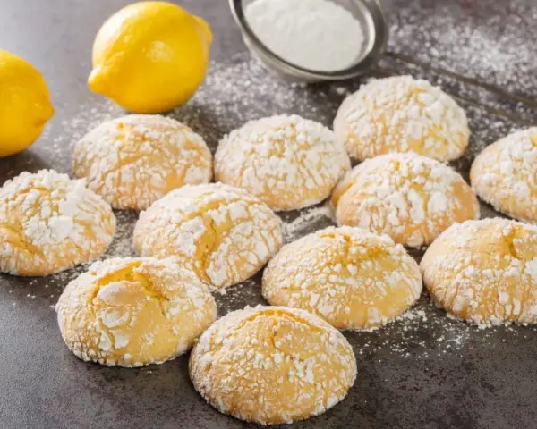 Deliziosi biscotti al limone spolverati di zucchero a velo, con limoni freschi sullo sfondo.