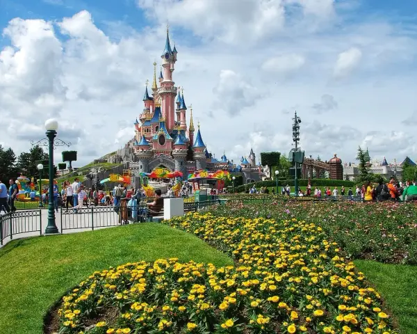 Disneyland Paris castle with colorful flowers and crowds of people.