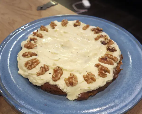 En saftig glutenfri morotskaka med krämig frosting och valnötter på en blå tallrik.