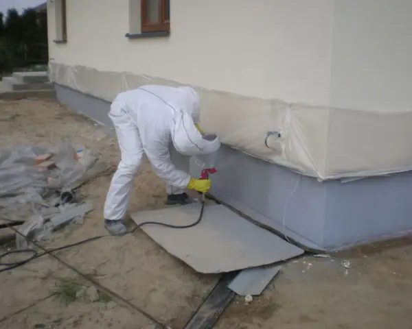 Pracownik w białym kombinezonie maluje fundamenty na kolor przypominający rubinowy.