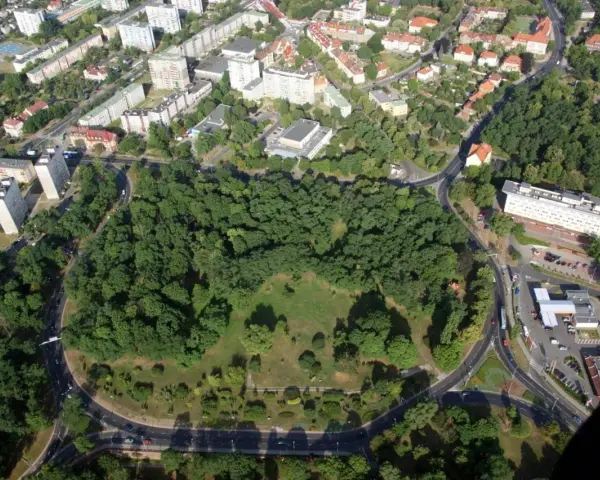 Widok z lotu ptaka na zielony park otoczony drogami, z budynkami mieszkalnymi w tle. To największe rondo w Polsce, które otacza serce miasta.