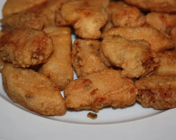 Un plato blanco lleno de trozos dorados y crujientes de japuta en adobo, listos para disfrutar.