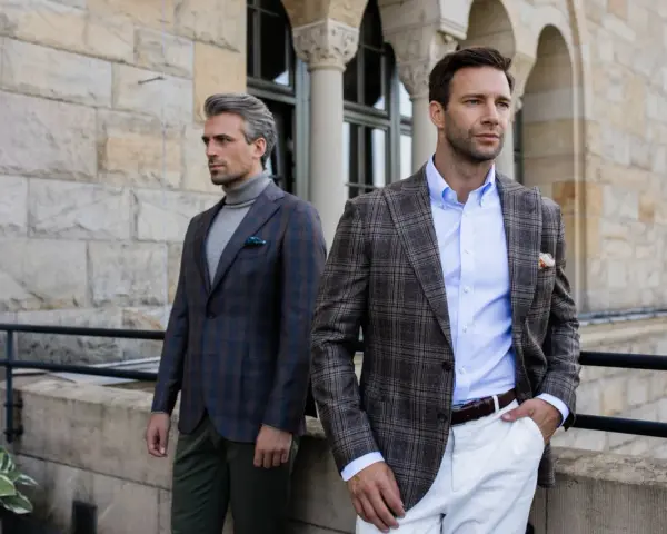 Dwóch eleganckich mężczyzn w marynarkach w kratę. Jeden ma szary golf, drugi błękitną koszulę. Stylowy mankiet co to?