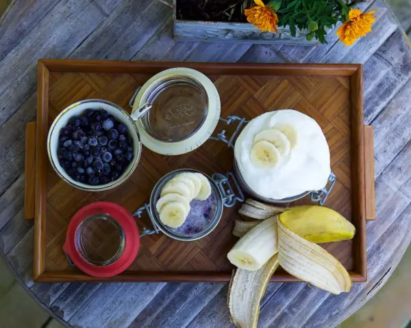 En bricka med ingredienser för sommarmat recept: blåbär, yoghurt, banan och en burk med bär och banan.