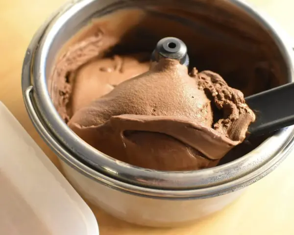 Un cucchiaio nero preleva una porzione di cremoso gelato fatto in casa al cioccolato da una gelatiera.
