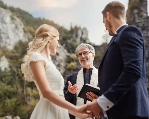 Piękna panna młoda i pan młody słuchają celebransa, który wygłasza cytaty na błogosławieństwo pary młodej podczas ceremonii na łonie natury.