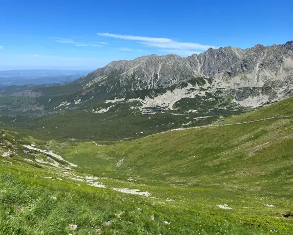 Widok na Tatry z zielonymi zboczami i skalistymi szczytami. W oddali widać budynki. Zastanawiasz się, ile km jest na Kasprowy Wierch?