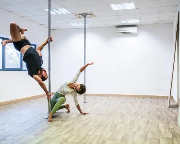 Para ćwiczy pole dance, pokazując efekty odchudzania. On wisi na rurze, ona kuca obok.