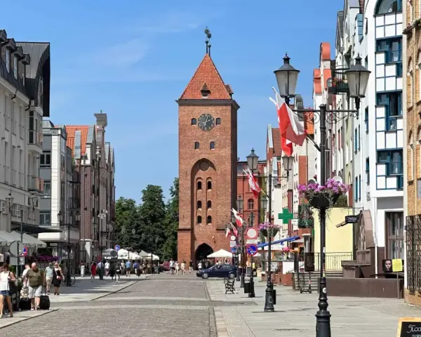 Ulica w Elblągu, z charakterystyczną wieżą i kolorowymi kamienicami. To najniżej położone miasto w Polsce, pełne urokliwych zakątków.