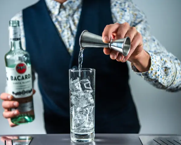 Barman nalewa rum Bacardi do szklanki z lodem, przygotowując Cuba Libre. Jaki rum do drinka? Bacardi Carta Blanca.