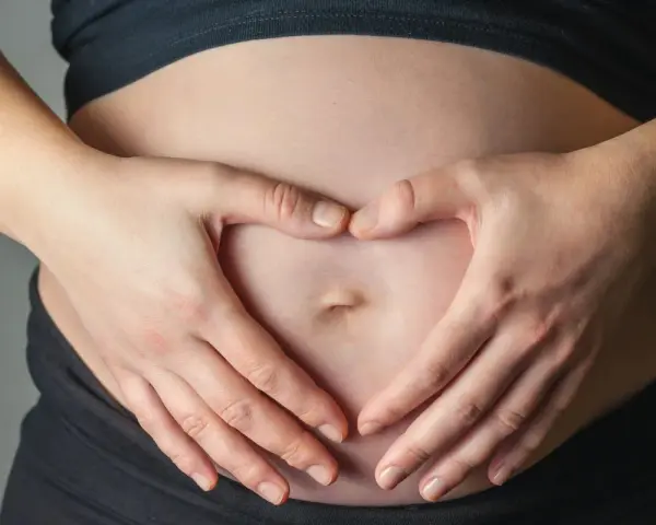Dłonie tworzą serce na brzuchu, symbolizując miłość i troskę o to, jak dziecko oddycha w brzuchu.