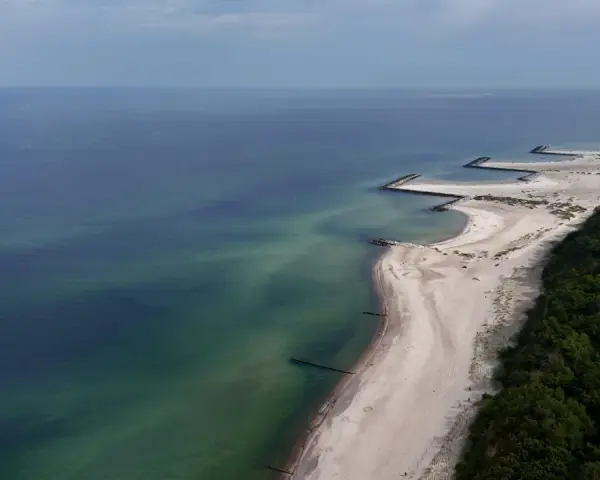 Plaża w Jarosławcu, zwana czasem "plażą dubaj", z kamiennymi falochronami i zielonym lasem.