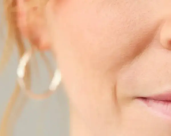 Nahaufnahme eines Gesichts mit sichtbarer Nasolabialfalte, die mit 40 Jahren typisch ist. Eine Frau mit dezentem Lächeln.
