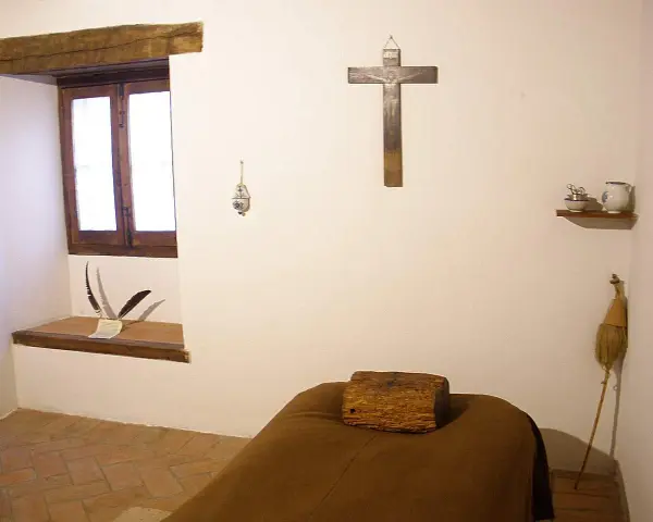 A monk's simple cell, showing where monks sleep: a narrow bed with a wooden block for a pillow, a crucifix, and a window.
