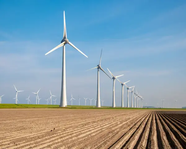 Rząd białych turbin wiatrowych na tle błękitnego nieba, nad zaoranym polem.