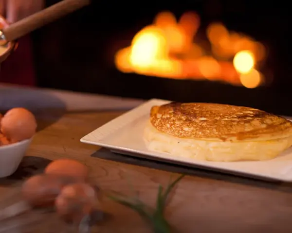 Une omelette mere poulard dorée et moelleuse, prête à être dégustée près d'un feu de cheminée. Des œufs frais sont visibles à côté.