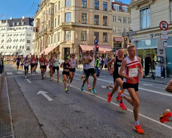 Corredores compiten en una media maratón en Europa, con edificios históricos y público animando.
