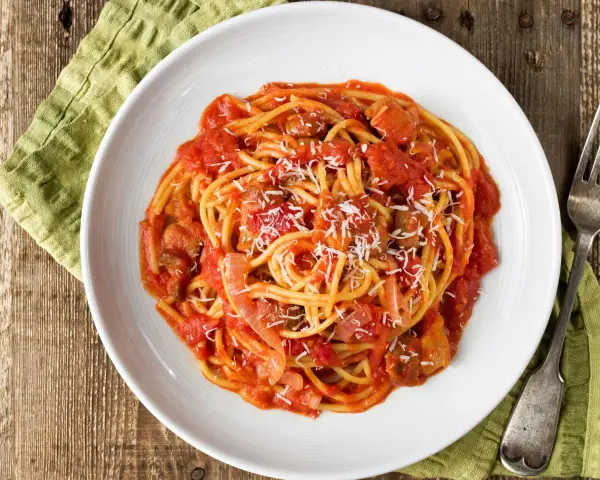 Spaghetti al pomodoro con pezzi di carne e cipolla, uno dei classici sughi per pasta, spolverati di parmigiano.