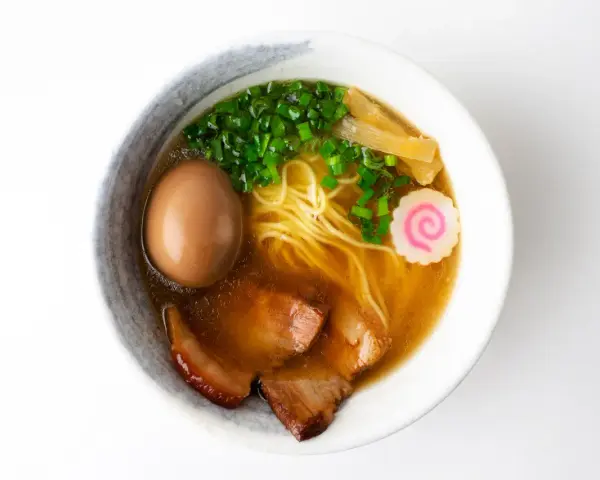 A miseczce shoyu ramen z makaronem, jajkiem, plastrami wieprzowiny, szczypiorkiem, bambusem i różową rybną kluską.