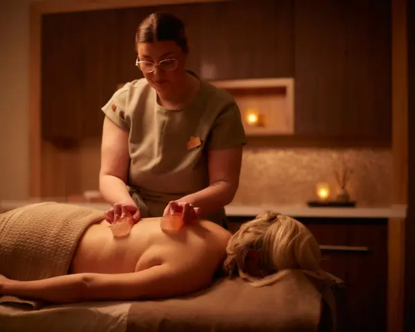 A therapist performs a Himalayan salt massage, placing warm salt stones on a client's back.