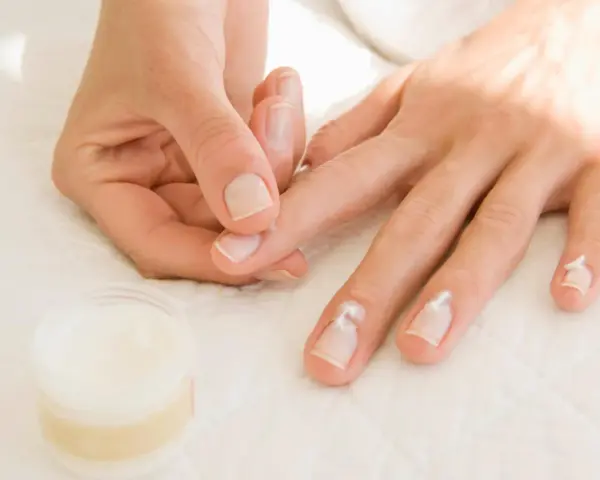 Application de crème pour hydrater la peau sèche autour des ongles.