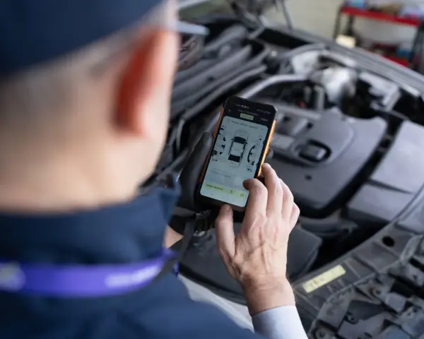 Mechanik sprawdza kody błędów DTC Renault na telefonie, analizując raport z pomiaru lakieru.