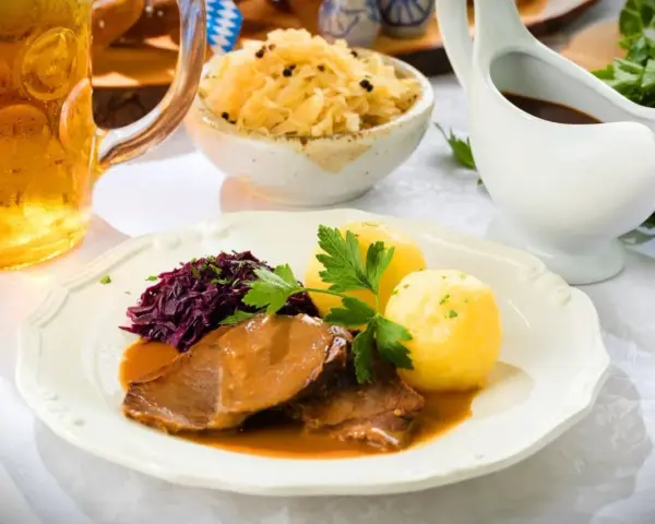 Deftiger Schweinebraten mit Klößen, Rotkohl und Sauerkraut. Dazu passt ein kühles Bier.