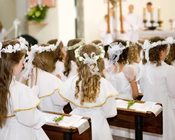 Dzieci w bieli, z wiankami na głowach, czekają na uroczystość. Piękne życzenia na komunie dla nich.