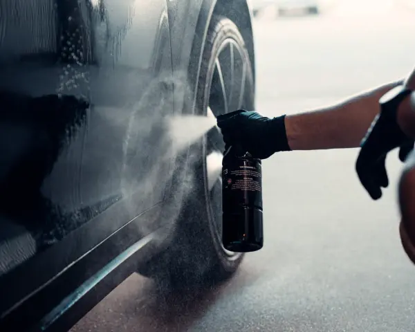 En hand med handske sprayar en bil för att ta bort dekaler.