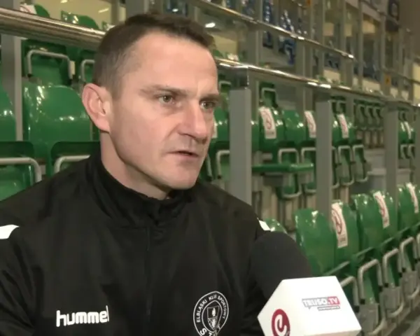 Marcin Pilch udziela wywiadu przed rzędem zielonych krzesełek na trybunach.