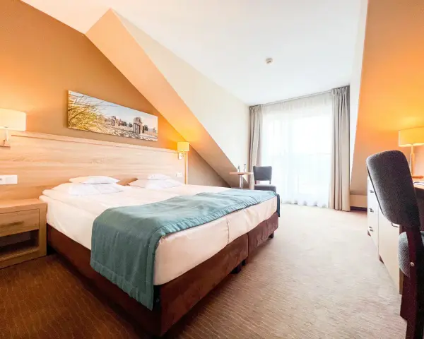 Przytulny pokój hotelowy z wygodnym łóżkiem, biurkiem i oknem. Idealne miejsce na nocleg tranzytowy, by odpocząć w podróży.