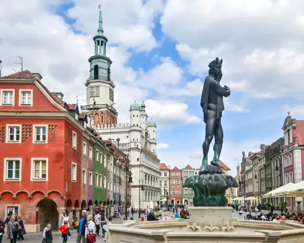 Pomnik króla na Rynku w Poznaniu, w tle kolorowe kamienice i ratusz.
