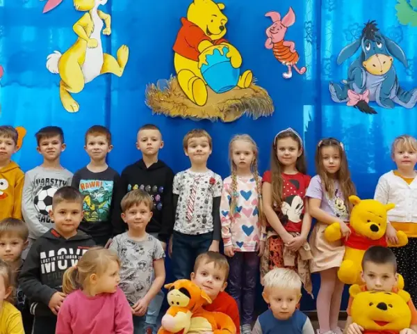 Dzieci pozują do zdjęcia z Kubusiem Puchatkiem i przyjaciółmi, świętując Dzień Kubusia Puchatka.