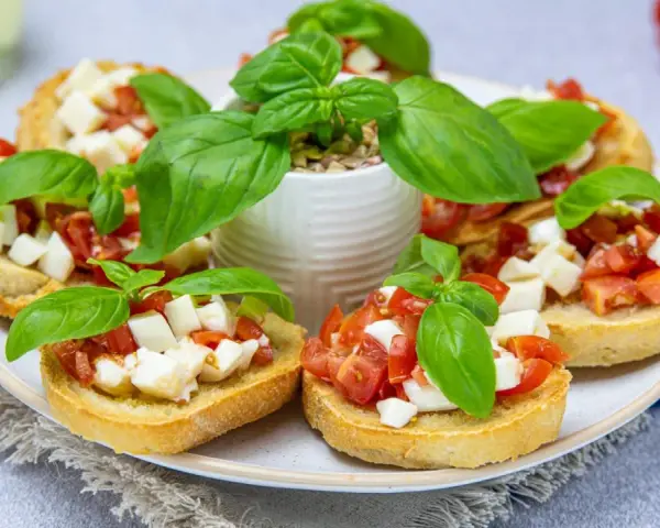 Bruschetta z pomidorami i mozzarellą – pyszny przepis na letnią przekąskę. Chrupiące grzanki z dodatkiem świeżej bazylii.