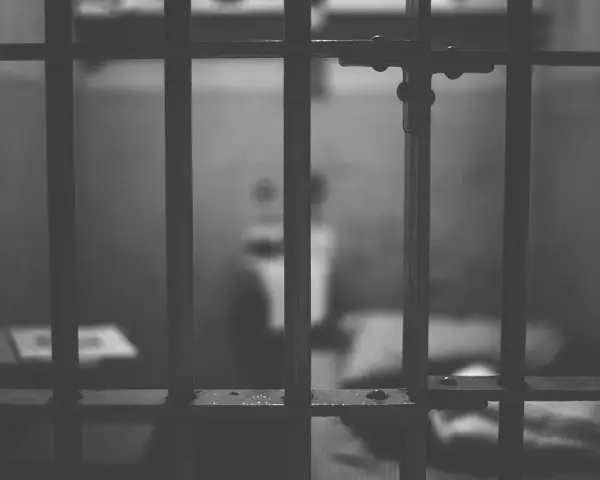 Widok przez kraty więzienne. W tle niewyraźna postać, symbolizująca nadzieję na wcześniejsze zatarcie skazania i nowe życie.