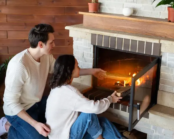 Pareja añade leña a la chimenea, creando un ambiente acogedor. Los insertables de madera se queman, iluminando la habitación.