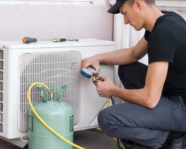 Técnico recargando gas aire acondicionado casa. Manómetro y tanque verde conectados a la unidad exterior.