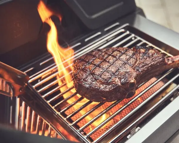 Ein saftiges Steak wird auf einem Gasgrill gegrillt, Flammen züngeln empor.