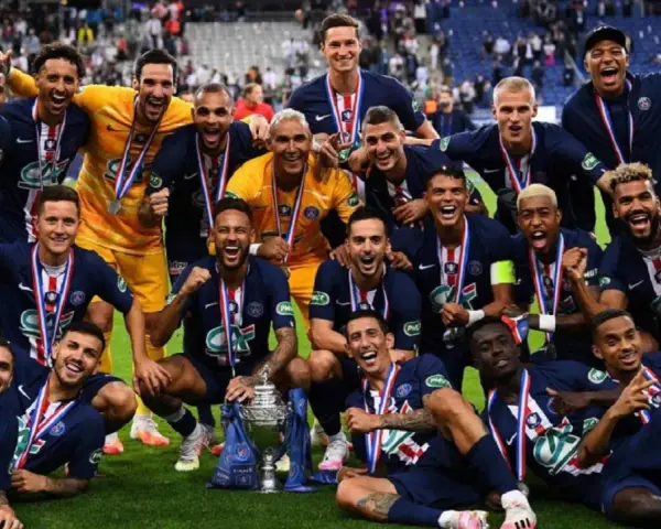 Un grupo de jugadores de Ligue 1 celebra con trofeos y medallas, sonriendo y vitoreando en el campo.