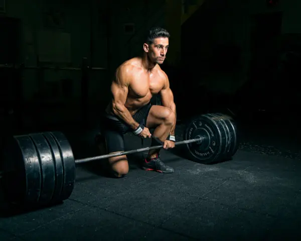 Un homme musclé s'apprête à soulever une barre chargée, profitant d'un temps de repos musculation dans une salle sombre.