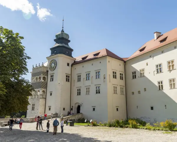 Zamek w Pieskowej Skale z charakterystyczną wieżą zegarową i renesansową attyką. Zwiedzający spacerują po dziedzińcu.