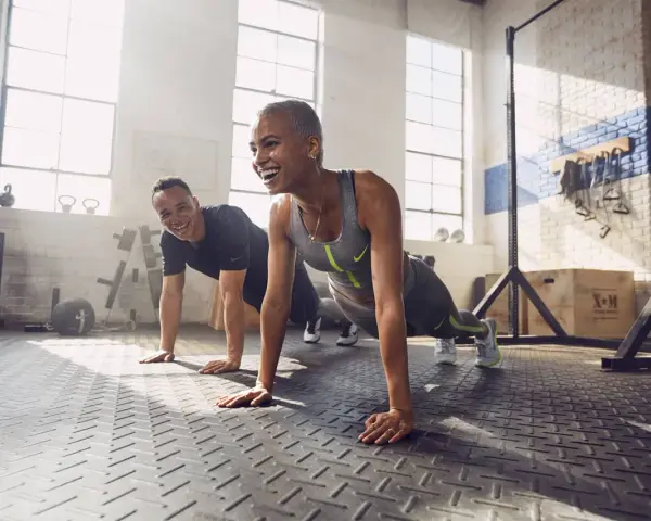 Coppia sorridente in palestra, che fa flessioni. Lo sport è un valido alleato contro la depressione, un modo per ritrovare energia e benessere.