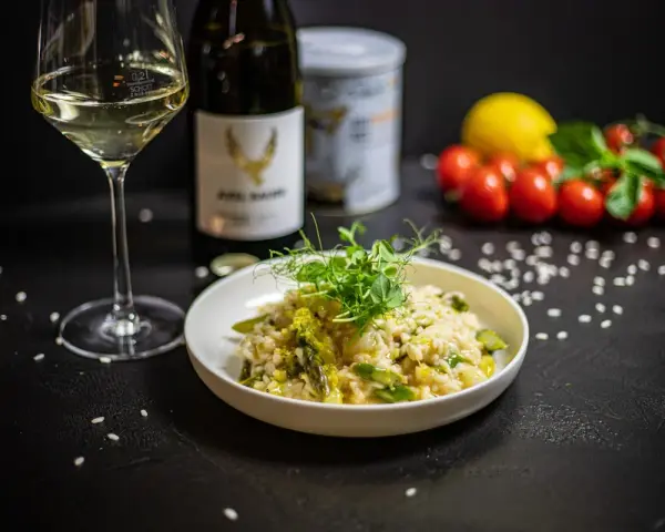 Aksamitne risotto z kurczakiem i szparagami, udekorowane kiełkami. Obok kieliszek białego wina i butelka.