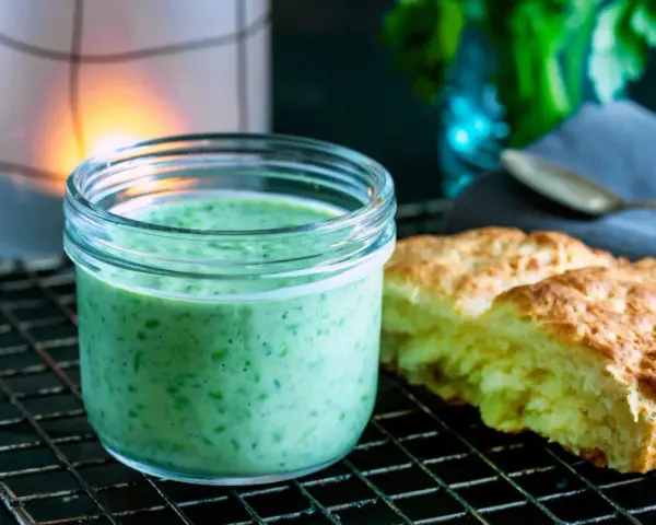 En burk med krämig, grön dressing, perfekt för ett grönt gudinnedressing recept. Bredvid ligger nybakade scones.