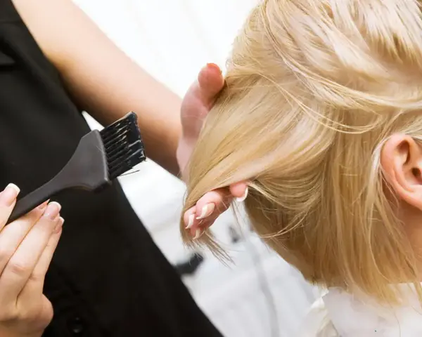 Fryzjerka wykonuje konturowanie włosów blond, nakładając farbę pędzelkiem.