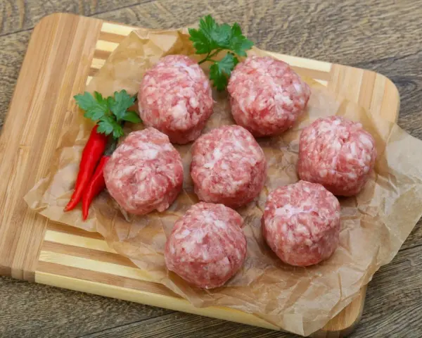 Surowe kotlety mielone keto, przyprawione papryczkami chili i natką pietruszki, leżą na papierze do pieczenia na desce.
