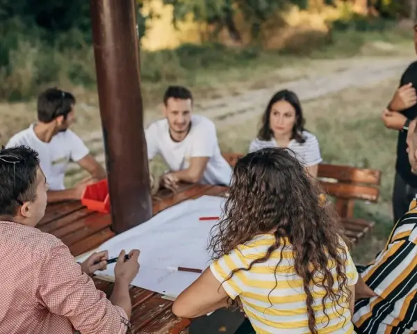 Un groupe discute autour d'une table en bois lors d'une sortie team building en plein air.