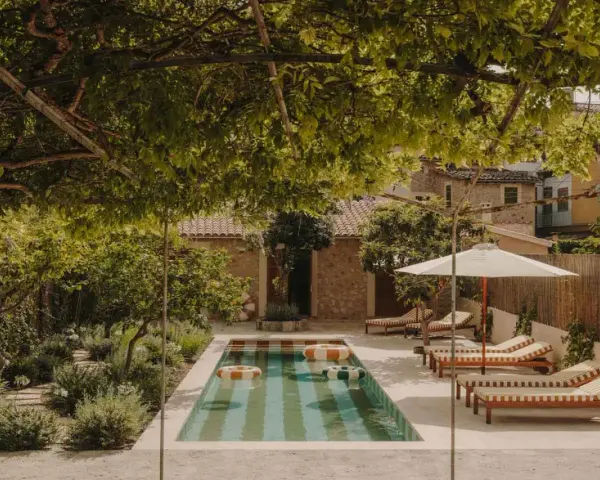 Piscina con galleggianti in un giardino rigoglioso, perfetto per idee piccoli giardini con piscina. Lettini e ombrellone invitano al relax.