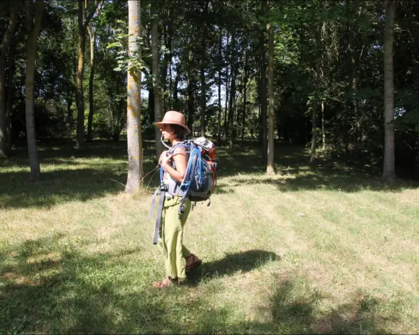 Une randonneuse avec un sac à dos et une poche à eau visible. Elle est dans une forêt, prête pour son aventure.