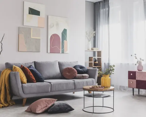 Divano grigio scuro con abbinamenti cuscini colorati e una coperta gialla. Tre quadri astratti decorano la parete.